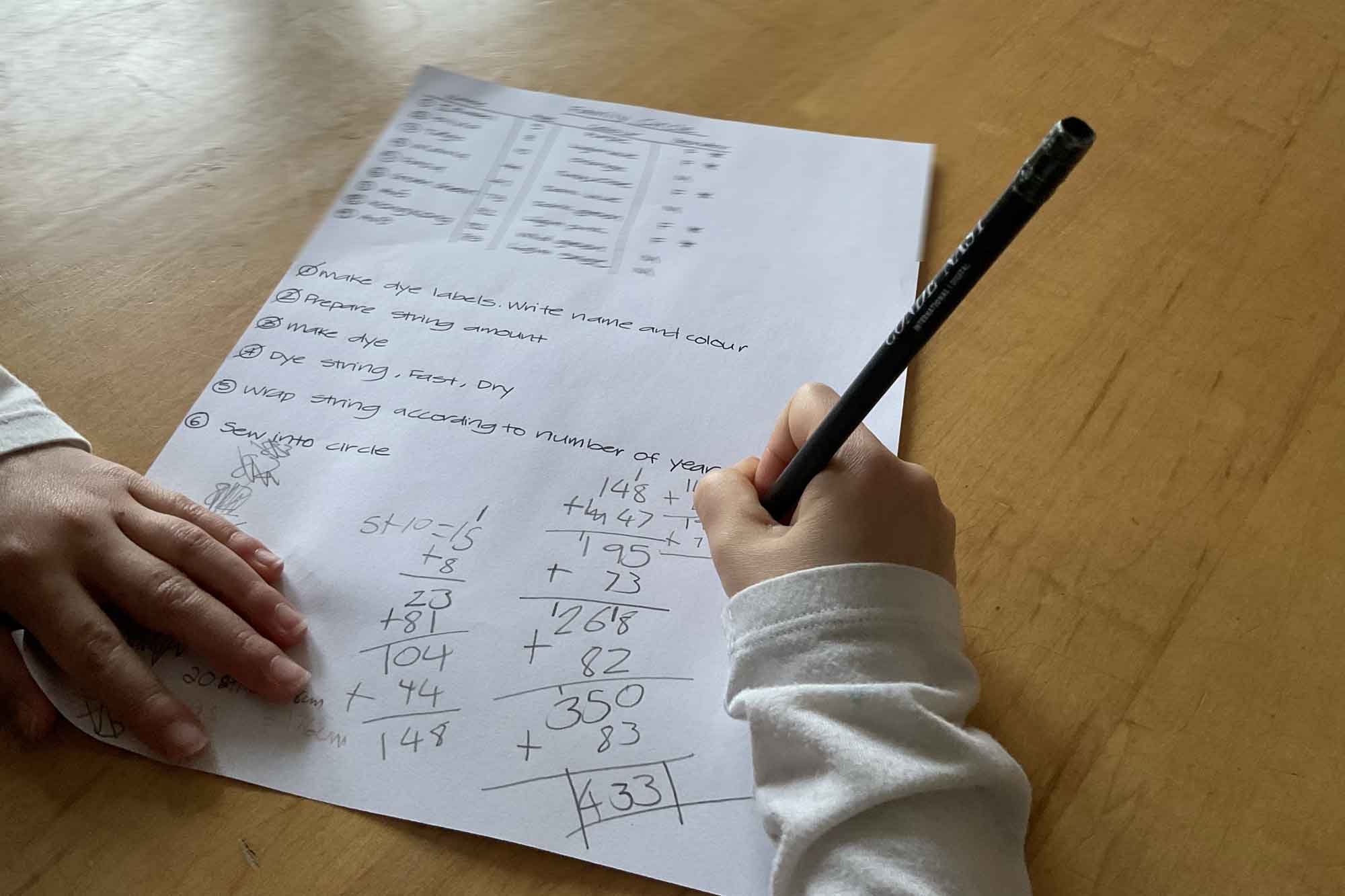 A child focused on writing on paper with a pencil, showcasing concentration in calculating mathematic formulas.