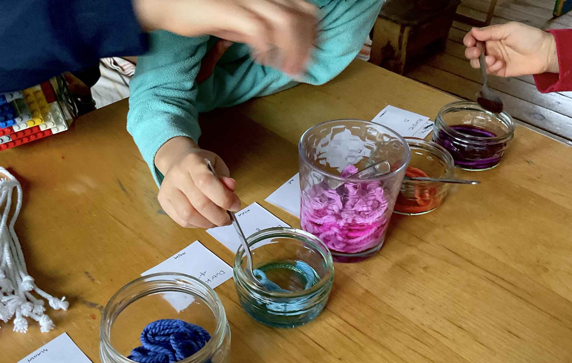  Three children putting string into colored liquid into jars with spoons, illustrating a fun moment of exploration.