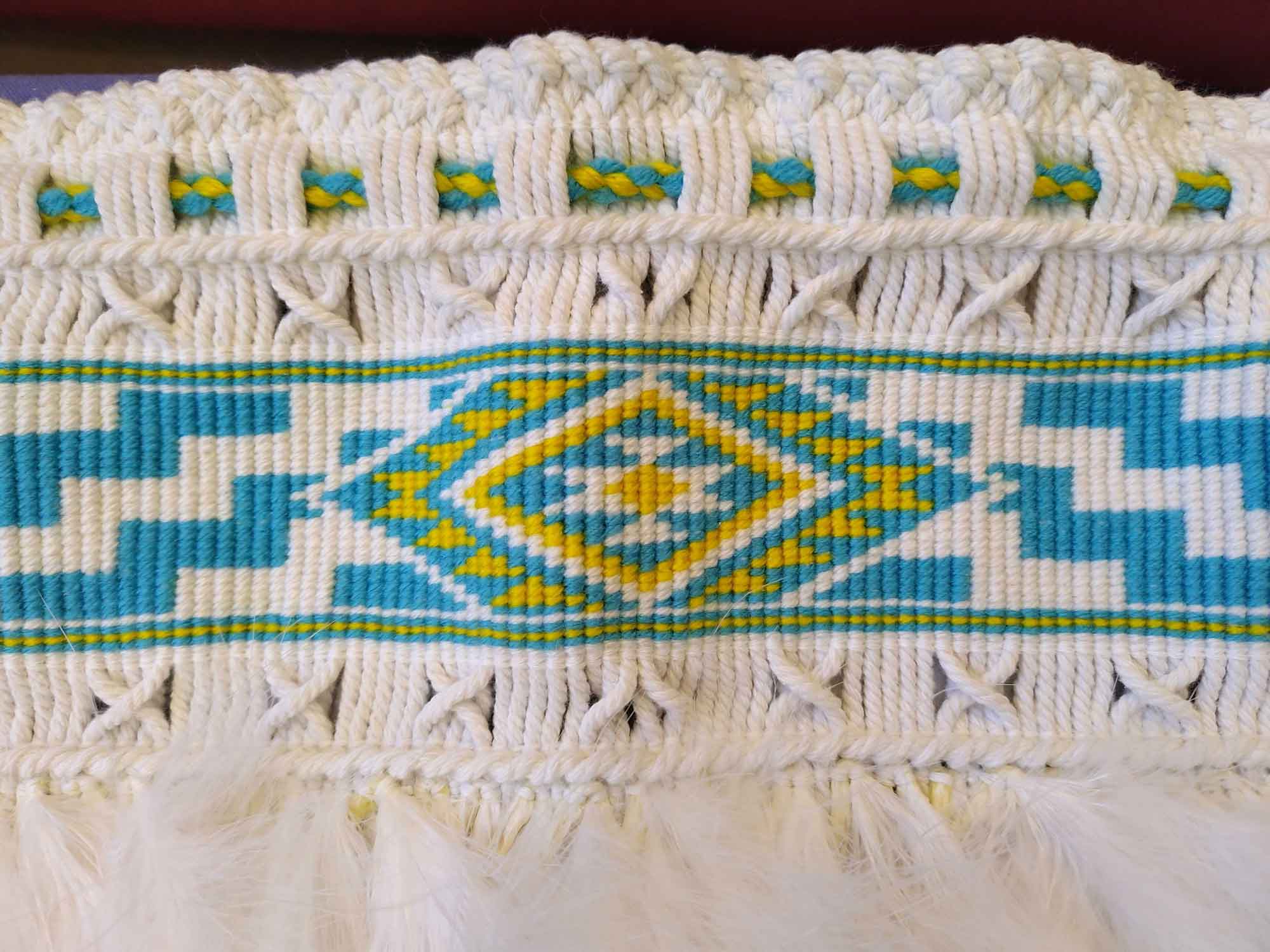 White blue and yellow pattern weaving with different stitches and white feathers at the bottom