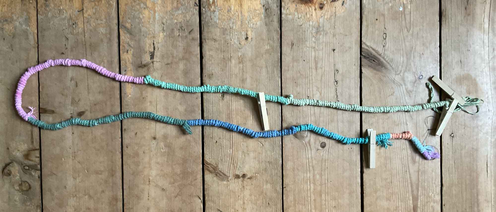 A long bright string of wrapped yarn in various colors rests on a wooden floor