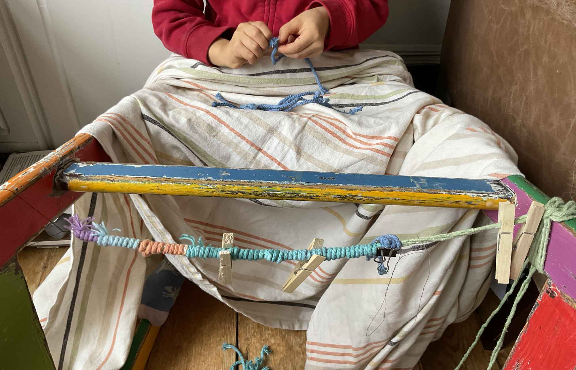 A child perched on a chair used as a frame for wrapping string, enveloped a blanket, unknotting string