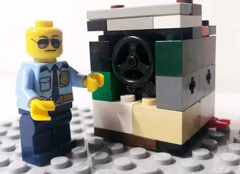 photograph of a lego person dressed in police uniform wearing sunglasses next to a lego constructed washing machine.